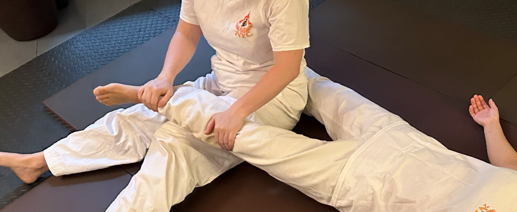 Martial arts instructor stretching student's leg on mat